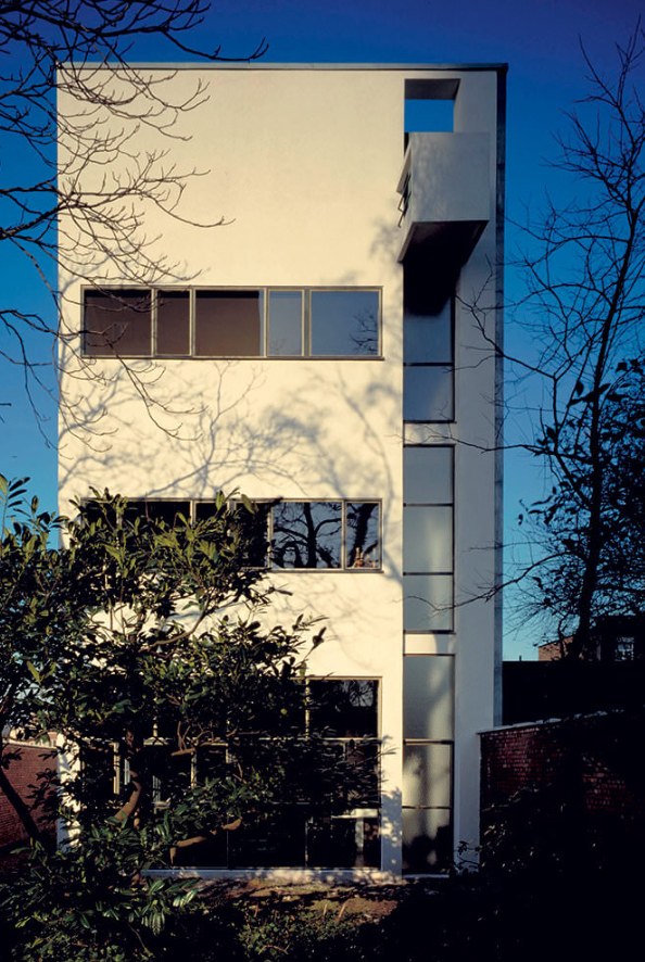 La fachada de la Casa Guiette a la calle, blanca y estrecha, contra
                un cielo azul de invierno: tres ventanas corridas, la franja
                vertical de la derecha y el vuelo del último piso.