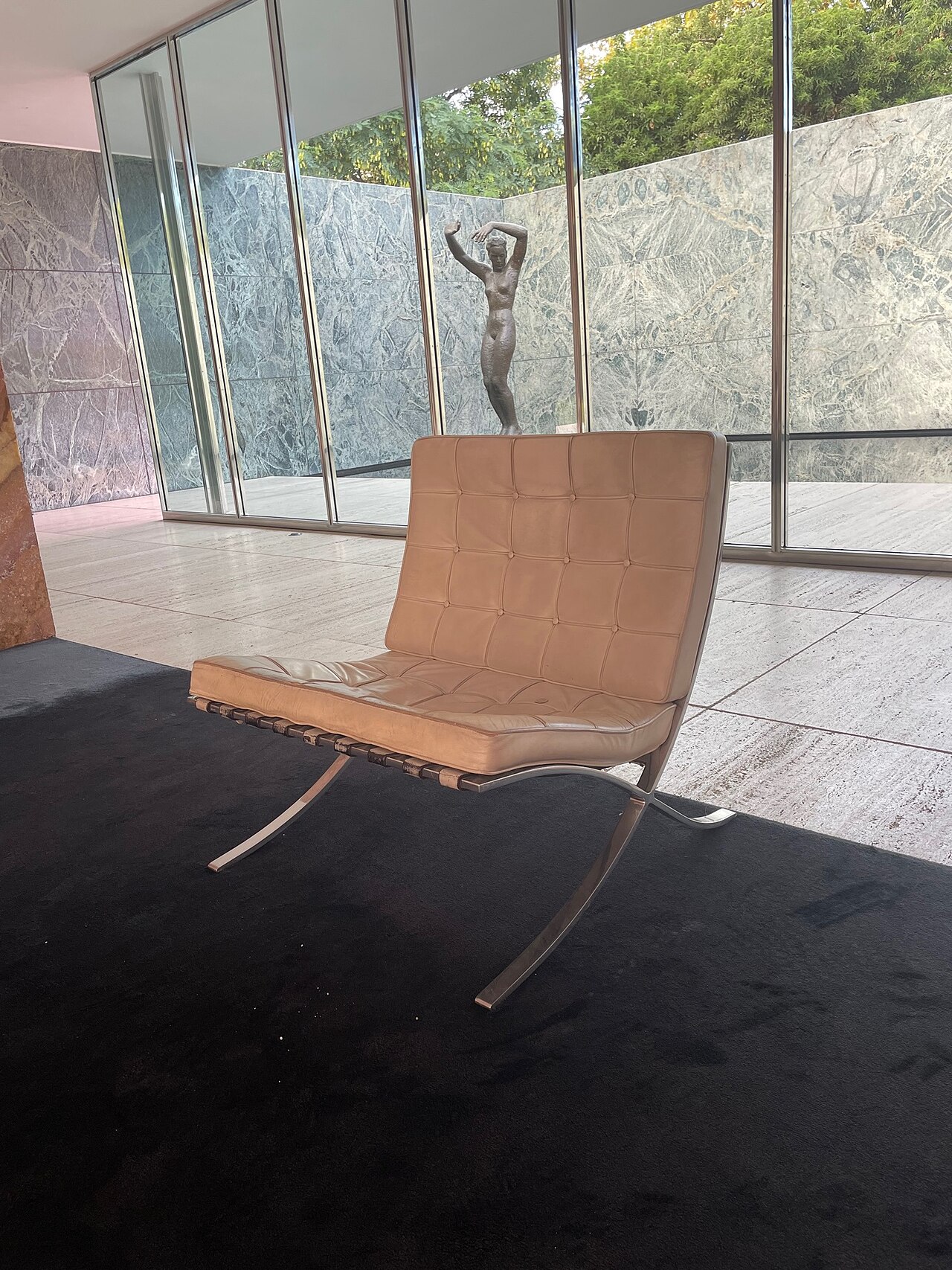 La silla Barcelona de Mies van der Rohe dentro del pabellón:
                    pletinas de acero cromado cruzadas en X y cojines de cuero
                    capitoné.